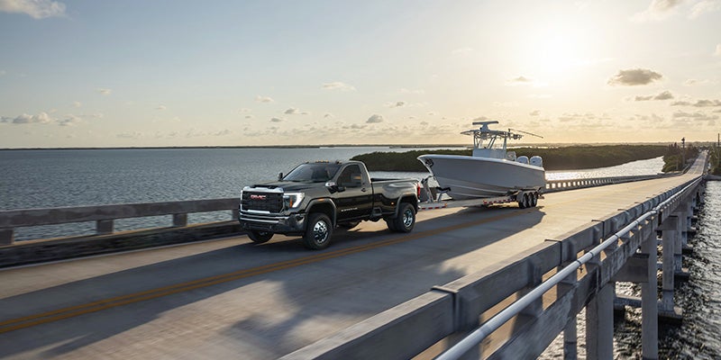 a grey 2024 GMC Sierra 3500 HD hauling a boat down a coastal highway with the sun setting in the background