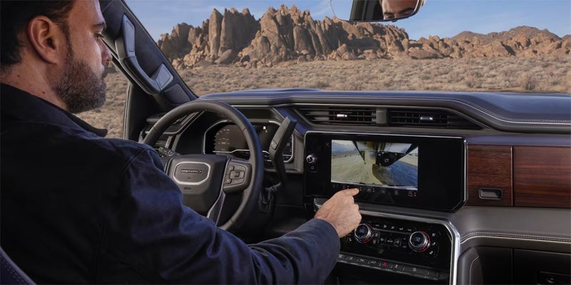Driver utilizing the safety features in a 2024 GMC Sierra 3500 HD with an arid landscape visible from the front windshield