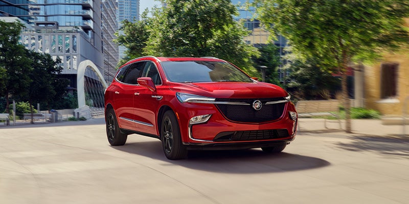 Red 2024 Buick Enclave driving down a road on a sunny day