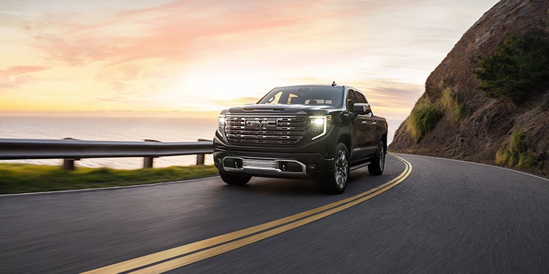 A black 2024 GMC Sierra 1500 driving down a coastal highway while the sun sets