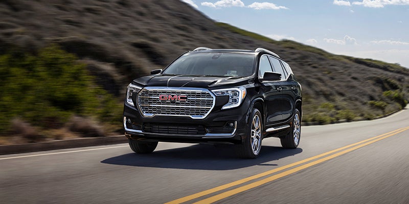 A black 2024 GMC Terrain driving down the road on a sunny day